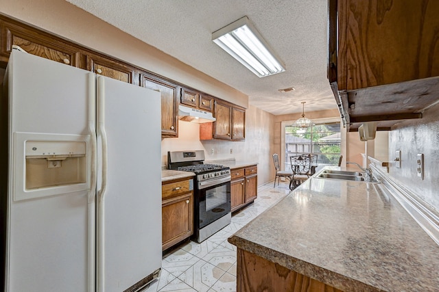 kitchen featuring sink, white refrigerator with ice dispenser, pendant lighting, a textured ceiling, and stainless steel range with gas stovetop