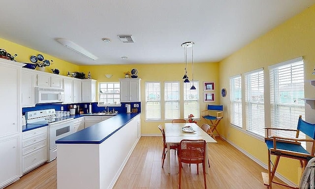 kitchen featuring white appliances, white cabinets, sink, hanging light fixtures, and light hardwood / wood-style floors