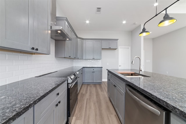 kitchen featuring sink, hanging light fixtures, stainless steel appliances, light hardwood / wood-style flooring, and decorative backsplash