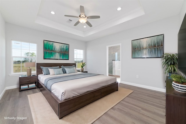 bedroom featuring ensuite bathroom, light hardwood / wood-style floors, ceiling fan, and a tray ceiling