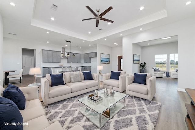 living room featuring a tray ceiling, ceiling fan, light hardwood / wood-style flooring, and ornamental molding