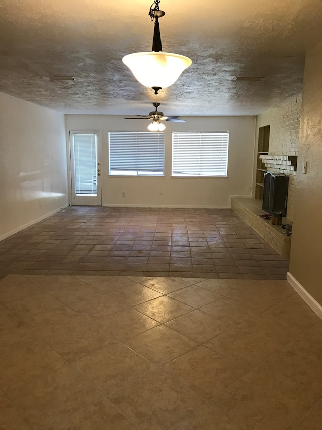 empty room featuring a textured ceiling, a brick fireplace, and ceiling fan