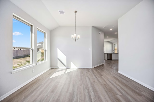 empty room with a notable chandelier, lofted ceiling, and light hardwood / wood-style flooring