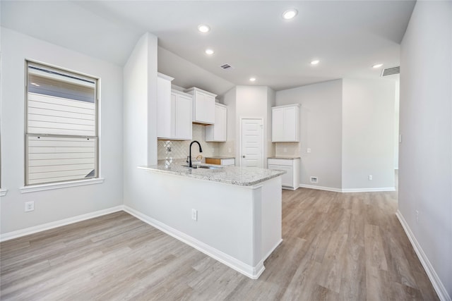 kitchen with white cabinets, sink, light hardwood / wood-style flooring, light stone counters, and kitchen peninsula