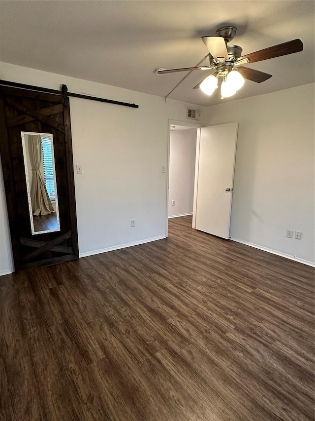 empty room featuring ceiling fan, a barn door, and dark wood-type flooring