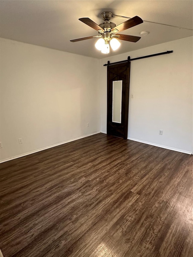 spare room with dark hardwood / wood-style flooring, a barn door, and ceiling fan