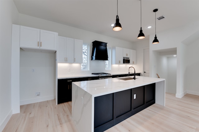 kitchen featuring white cabinetry, sink, a center island with sink, custom exhaust hood, and appliances with stainless steel finishes