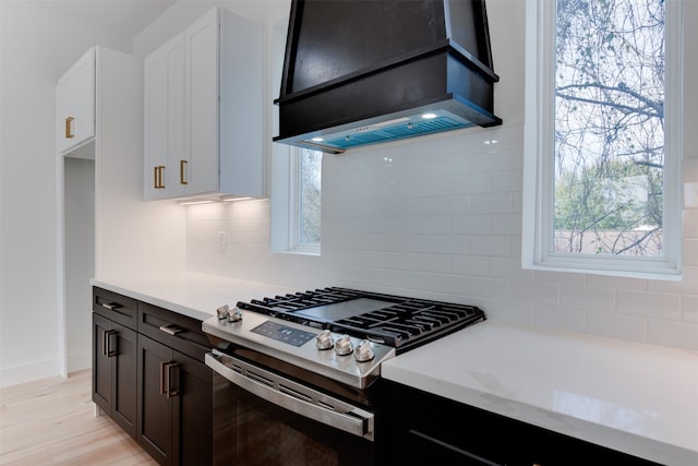 kitchen featuring tasteful backsplash, stainless steel gas range oven, custom range hood, light hardwood / wood-style floors, and white cabinetry