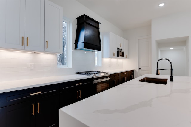 kitchen featuring light stone countertops, premium range hood, stainless steel appliances, sink, and white cabinetry