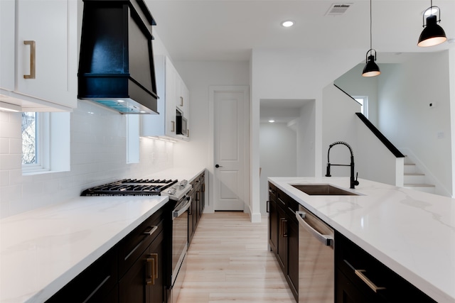 kitchen featuring appliances with stainless steel finishes, custom range hood, sink, pendant lighting, and white cabinetry