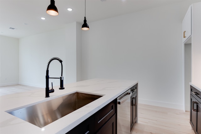 kitchen with light stone countertops, dishwasher, sink, light hardwood / wood-style flooring, and pendant lighting