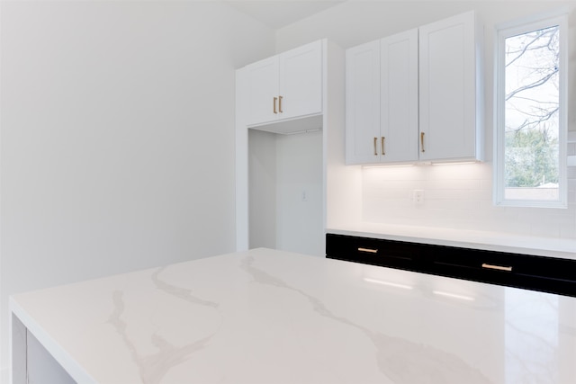 kitchen featuring white cabinets, backsplash, light stone counters, and a healthy amount of sunlight