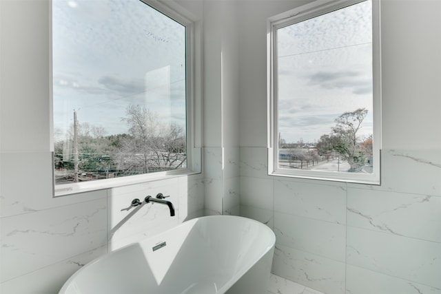 bathroom with a bathing tub, a healthy amount of sunlight, and tile walls