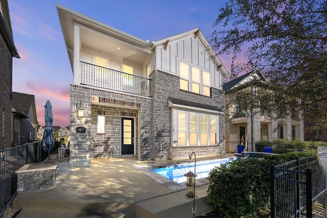 back house at dusk featuring a balcony, a fenced in pool, and a patio