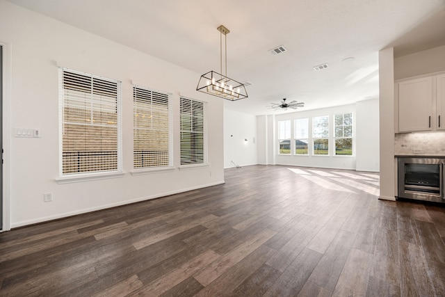 unfurnished living room with ceiling fan with notable chandelier, beverage cooler, and dark hardwood / wood-style floors