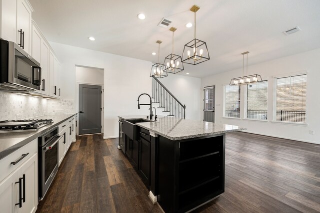 kitchen featuring appliances with stainless steel finishes, dark hardwood / wood-style flooring, a kitchen island with sink, decorative light fixtures, and white cabinets