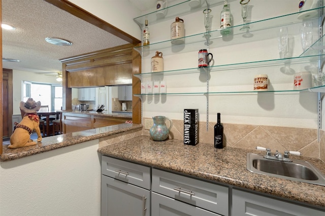 kitchen featuring ceiling fan, sink, tasteful backsplash, dark stone counters, and a textured ceiling