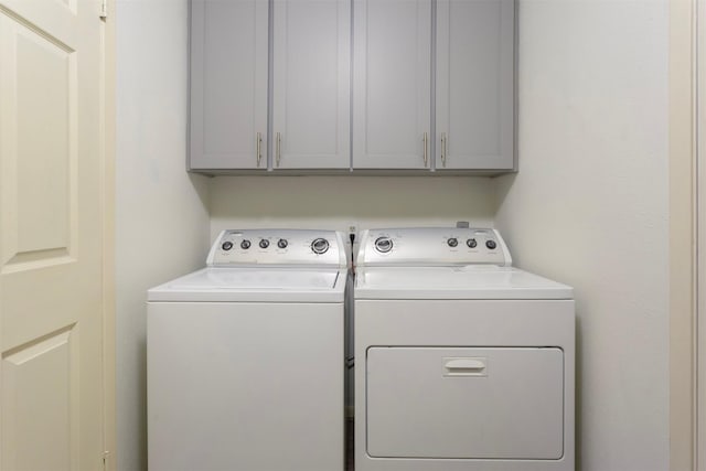 clothes washing area with washer and clothes dryer and cabinets