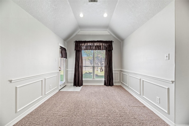 empty room with light colored carpet, lofted ceiling, and a textured ceiling