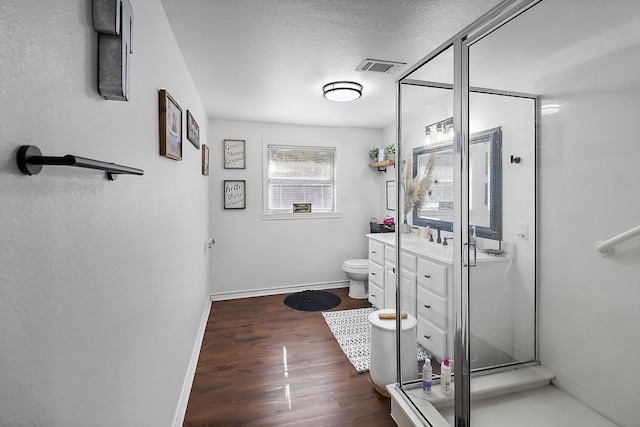 bathroom featuring a textured ceiling, vanity, a shower with door, hardwood / wood-style flooring, and toilet