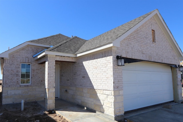 view of property exterior featuring a garage, brick siding, and roof with shingles