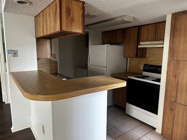 kitchen featuring a textured ceiling, kitchen peninsula, light tile patterned floors, and white appliances