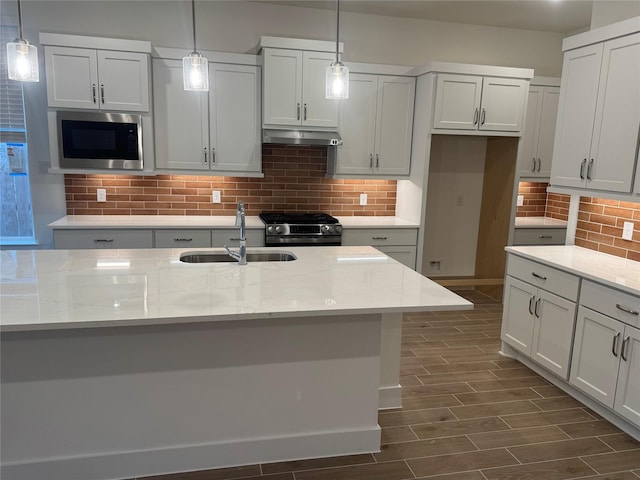 kitchen with light stone countertops, appliances with stainless steel finishes, sink, and decorative light fixtures