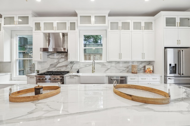 kitchen featuring appliances with stainless steel finishes, light stone counters, sink, wall chimney range hood, and white cabinets