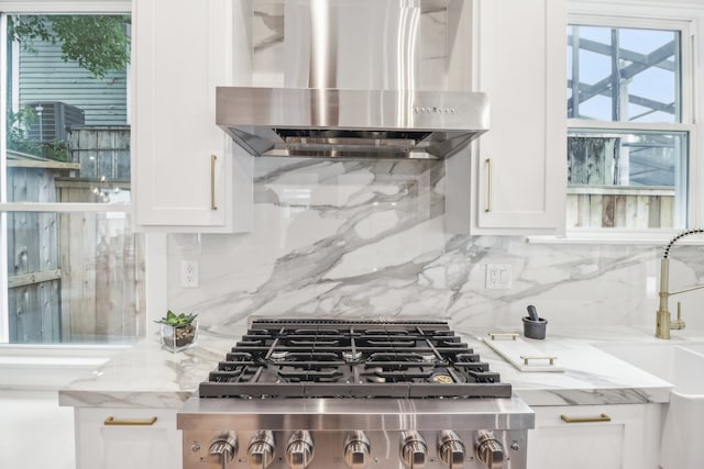 kitchen with light stone countertops, tasteful backsplash, white cabinets, and wall chimney exhaust hood