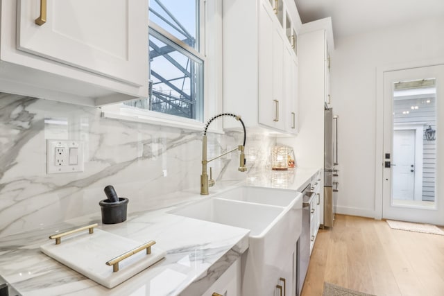 kitchen with light wood-type flooring, tasteful backsplash, light stone counters, sink, and white cabinets