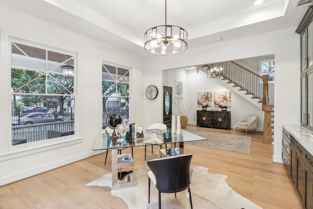 dining area featuring light hardwood / wood-style floors, a tray ceiling, and a notable chandelier