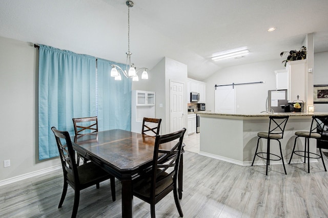 dining room with a barn door, light hardwood / wood-style floors, and vaulted ceiling