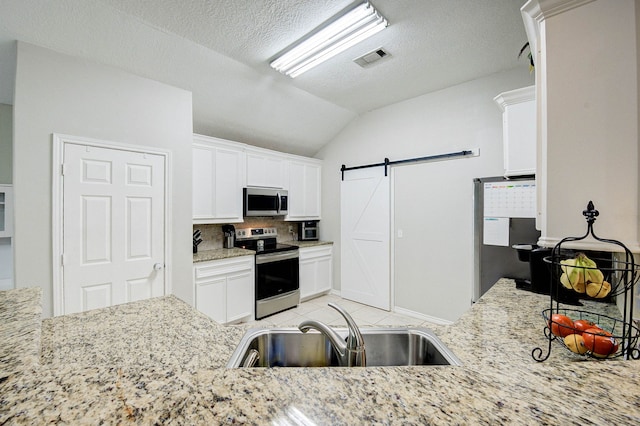 kitchen with white cabinetry, light stone countertops, stainless steel appliances, a barn door, and vaulted ceiling