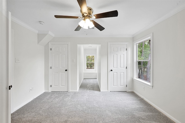 unfurnished bedroom featuring ceiling fan, light colored carpet, crown molding, and multiple windows