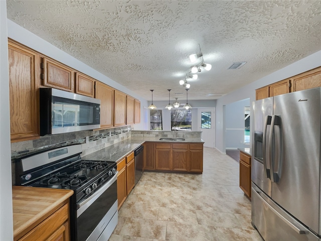 kitchen featuring kitchen peninsula, hanging light fixtures, a textured ceiling, and appliances with stainless steel finishes