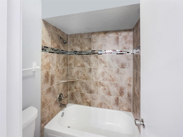 bathroom featuring a textured ceiling, toilet, and tiled shower / bath