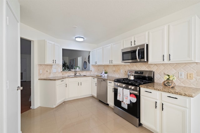 kitchen with white cabinets, appliances with stainless steel finishes, light stone counters, and sink