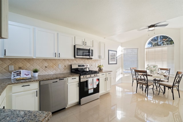 kitchen featuring decorative backsplash, stainless steel appliances, dark stone countertops, white cabinets, and lofted ceiling