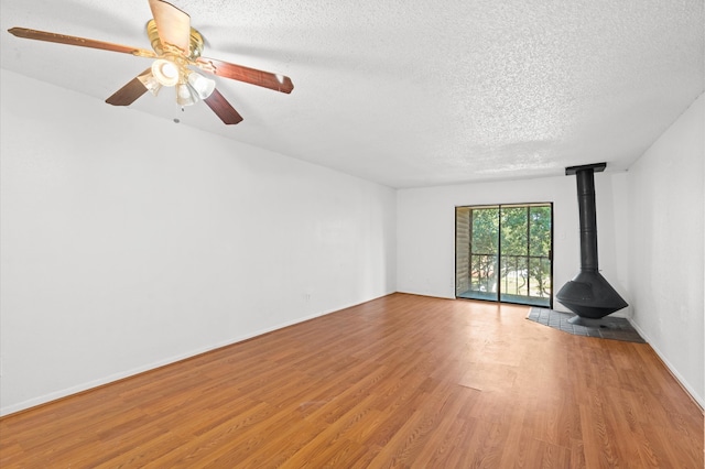 unfurnished living room featuring a textured ceiling, light wood-type flooring, a wood stove, and ceiling fan