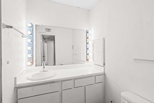 bathroom with a textured ceiling, vanity, and toilet