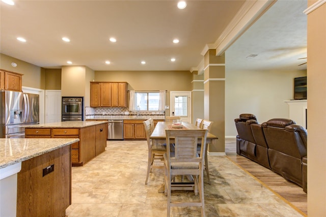 kitchen featuring stainless steel appliances, tasteful backsplash, light stone counters, a kitchen island, and ornamental molding