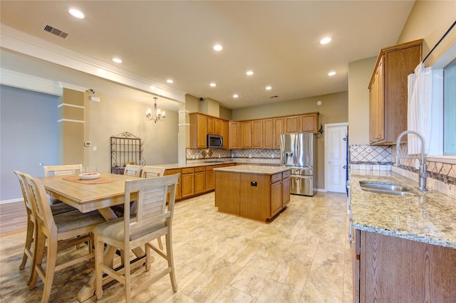 kitchen with sink, tasteful backsplash, light stone counters, a kitchen island, and appliances with stainless steel finishes