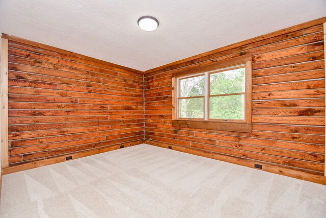 spare room with carpet flooring, a textured ceiling, and wood walls