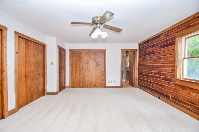 unfurnished bedroom featuring multiple closets, ceiling fan, and light carpet