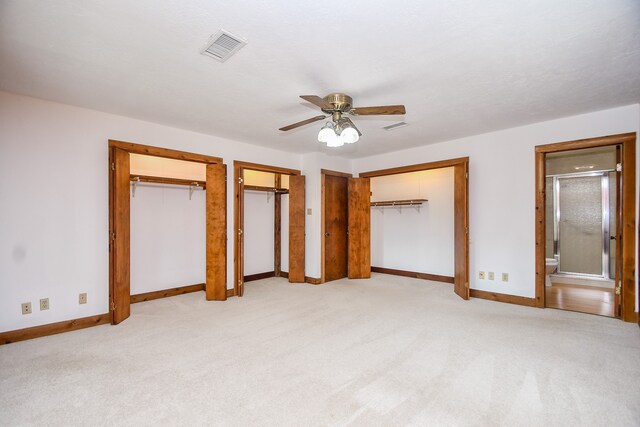 unfurnished bedroom with multiple closets, ceiling fan, ensuite bath, and light colored carpet