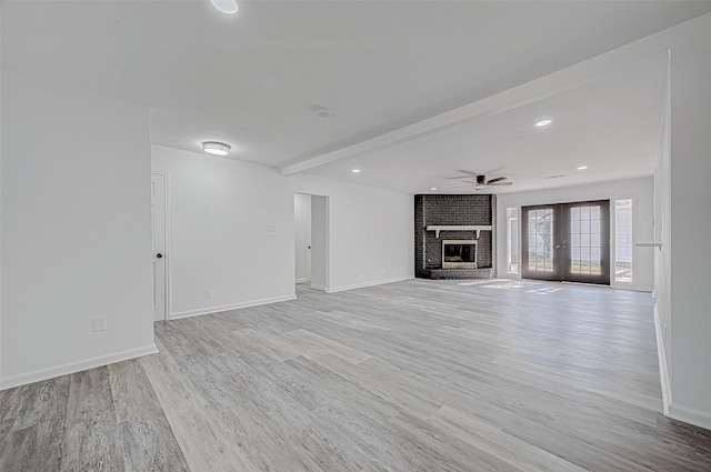 unfurnished living room featuring ceiling fan, french doors, a brick fireplace, beamed ceiling, and light wood-type flooring