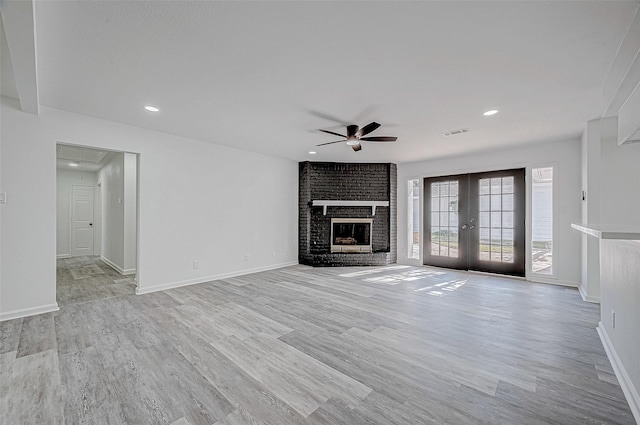 unfurnished living room featuring a fireplace, ceiling fan, light hardwood / wood-style flooring, and french doors