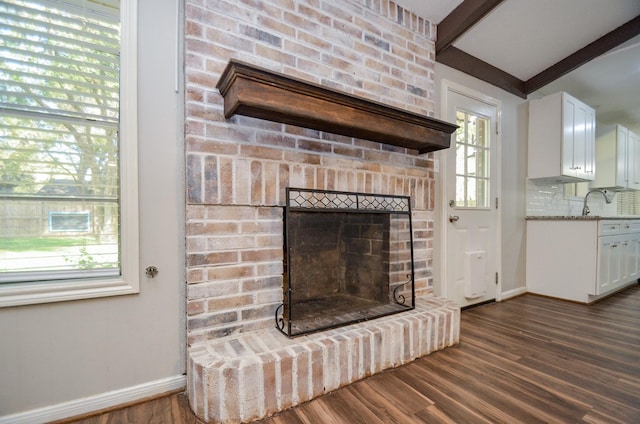 unfurnished living room featuring sink, dark hardwood / wood-style flooring, beamed ceiling, and a brick fireplace