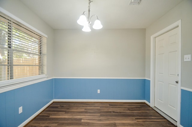 spare room with dark wood-type flooring and an inviting chandelier