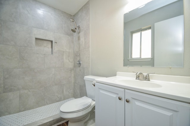 bathroom featuring a tile shower, vanity, and toilet